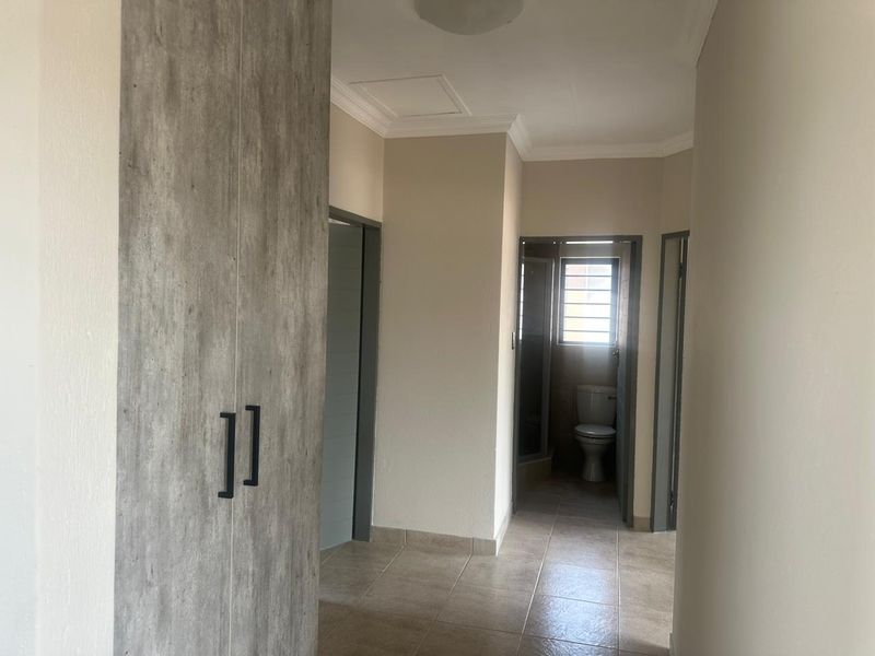 A clean, neutral-toned hallway featuring tiled flooring, built-in storage cabinetry, and access to an adjacent bathroom.