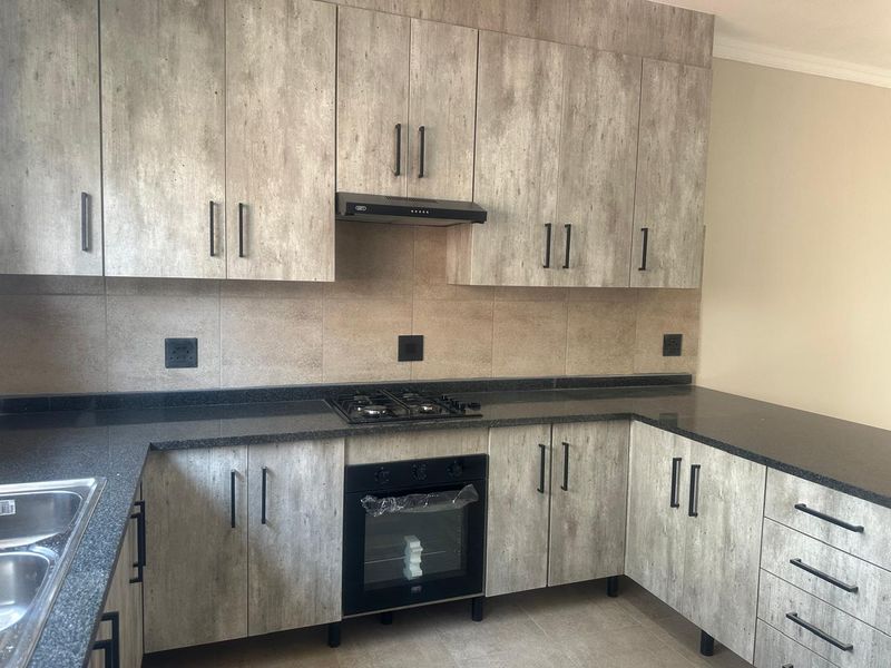 Modern kitchen featuring wood-look cabinetry, dark granite countertops, a gas hob, built-in oven, and a double bowl sink.