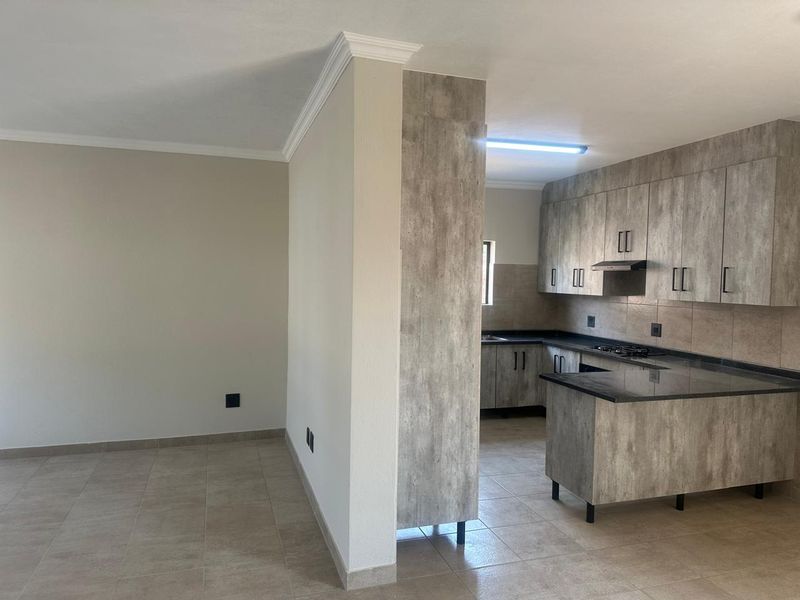 Open-plan living area featuring a modern kitchen with wood-look cabinetry, granite countertops, and a gas hob, finished with neutral floor tiles.