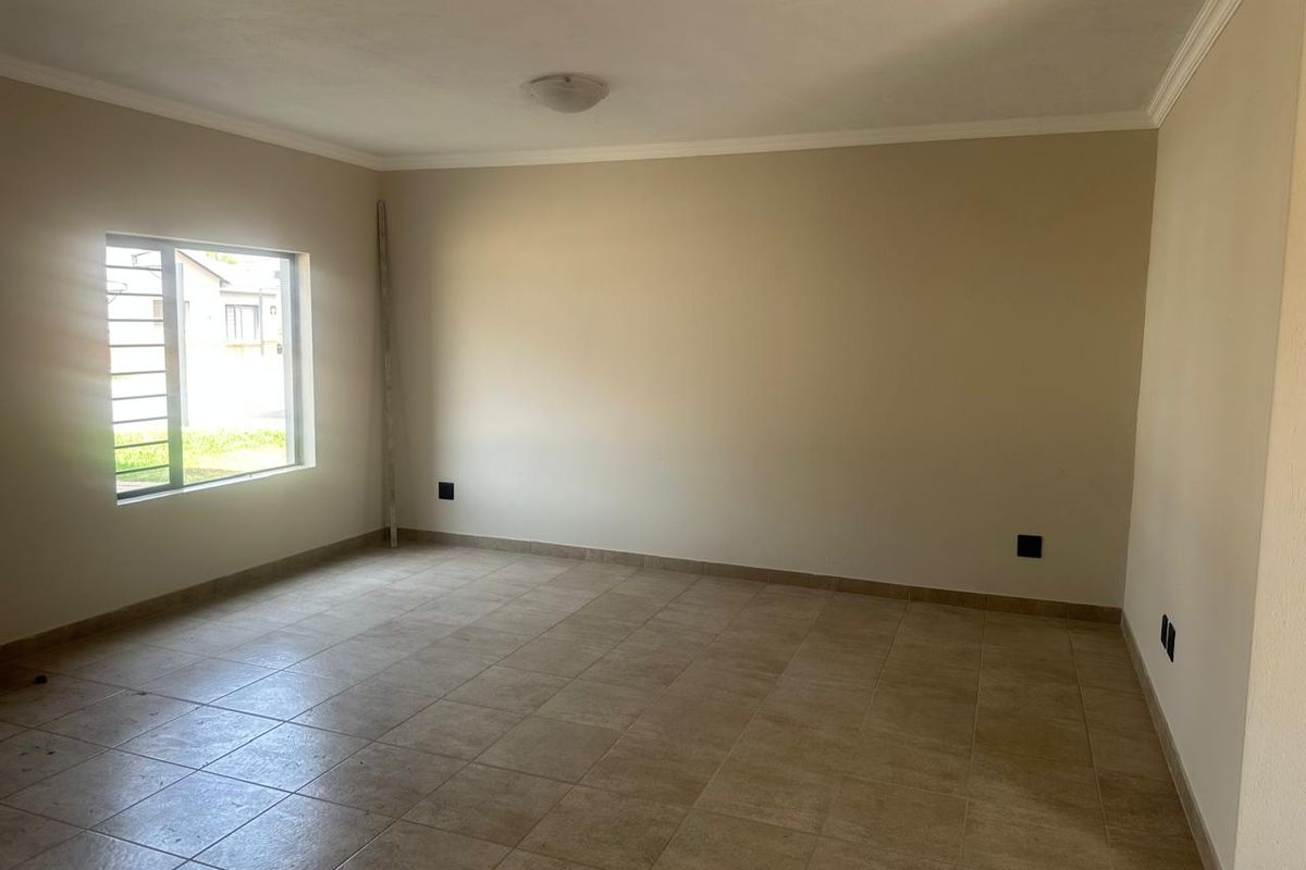 A spacious, empty living area featuring neutral tiled flooring, clean walls, and a window with security bars, offering a blank canvas for personalization.