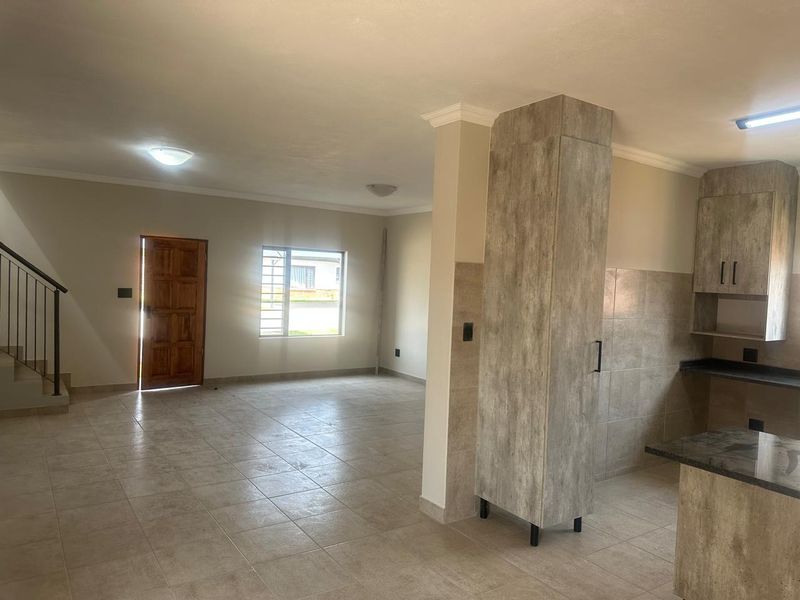 Spacious open-plan living area featuring tiled floors, a modern kitchen with built-in cabinetry, and a staircase leading to the upper level.