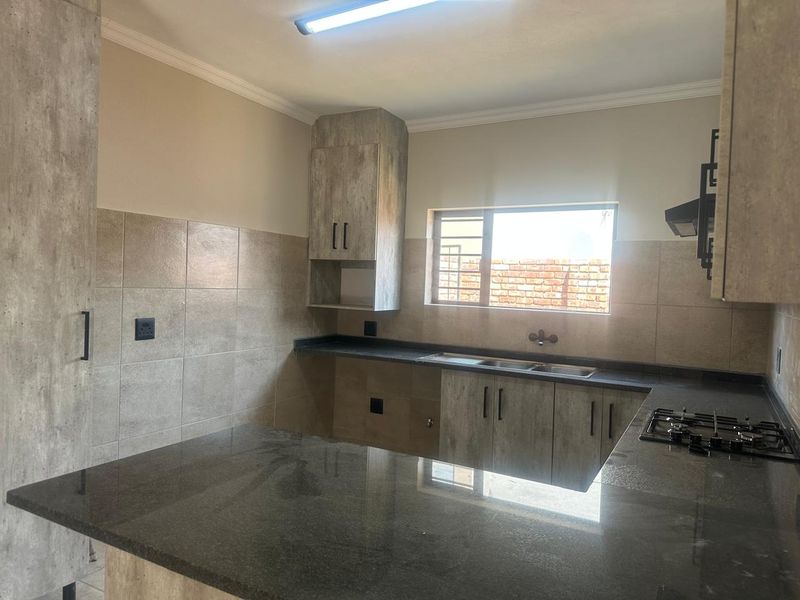 A functional kitchen featuring modern grey-toned cabinetry, granite countertops, a built-in gas hob, and a tiled backsplash, offering a clean and practical workspace.