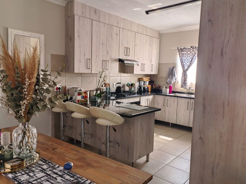 A functional kitchen featuring light wood-grain cabinetry, granite countertops, a breakfast bar, and a gas hob with an integrated extractor fan.