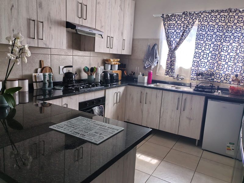 A functional kitchen featuring light wood-grain cabinetry, dark granite countertops, a gas hob with extractor, and tiled flooring with a double basin sink.
