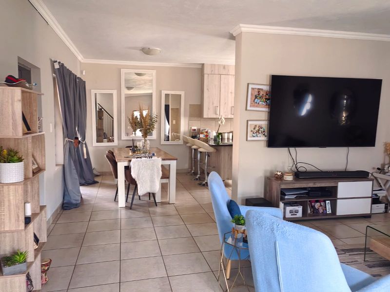 Open-plan living and dining area featuring tiled flooring, neutral walls, and a connected kitchen space with breakfast bar seating.