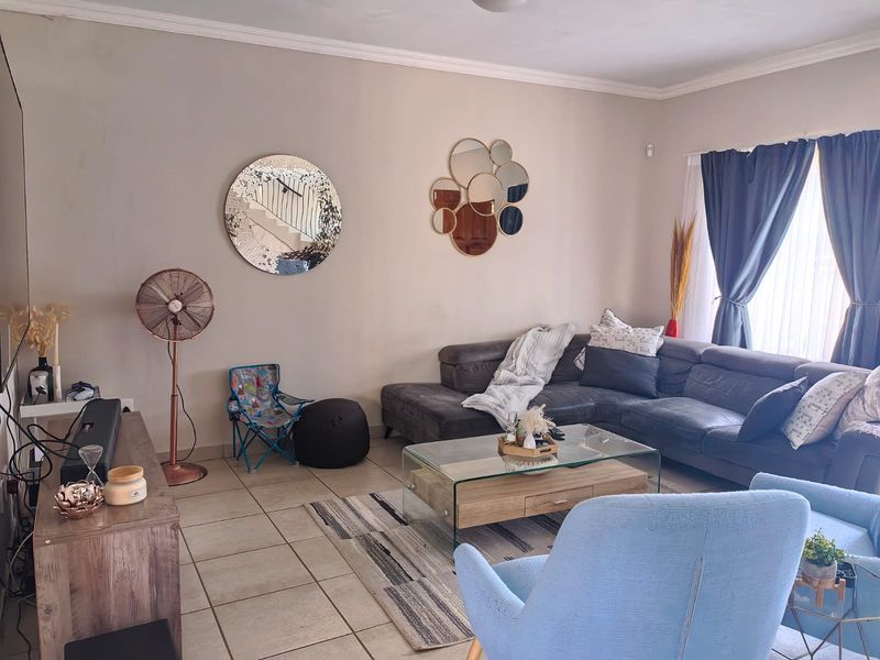A comfortable living room featuring neutral wall tones, tiled flooring, and decorative ceiling cornicing, providing a functional and inviting space.