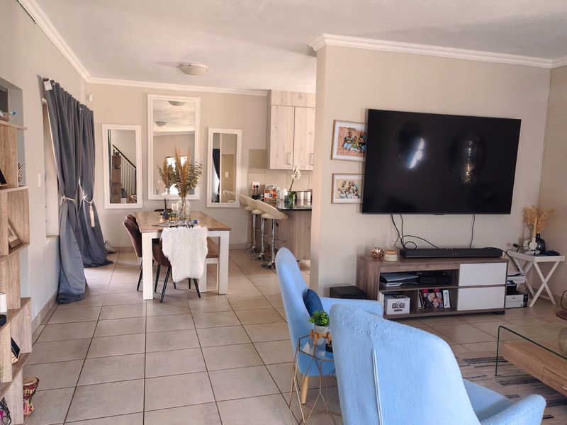 Open-plan living and dining area featuring tiled flooring, crown molding, and a functional kitchen with a breakfast bar.