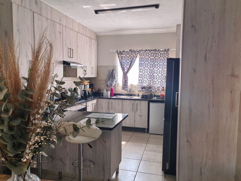 A functional kitchen featuring light wood-grain cabinetry, dark laminate countertops, a breakfast nook, and tiled flooring, providing a practical and well-organized cooking space.