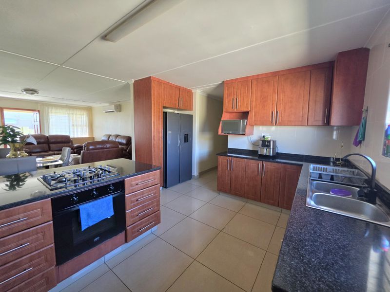 Open-plan kitchen featuring wood-finish cabinetry, granite countertops, gas hob, and integrated oven, flowing into a spacious living area with tiled flooring throughout.