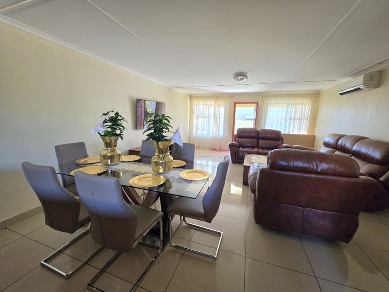 Spacious open-plan living and dining area featuring neutral tiled flooring and a wall-mounted air conditioning unit.
