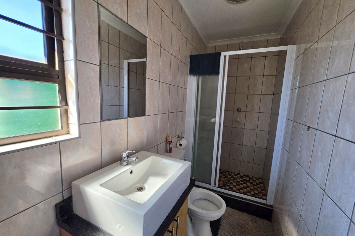 A functional bathroom featuring a vanity basin, a separate shower enclosure, and a toilet, finished with neutral wall tiling.
