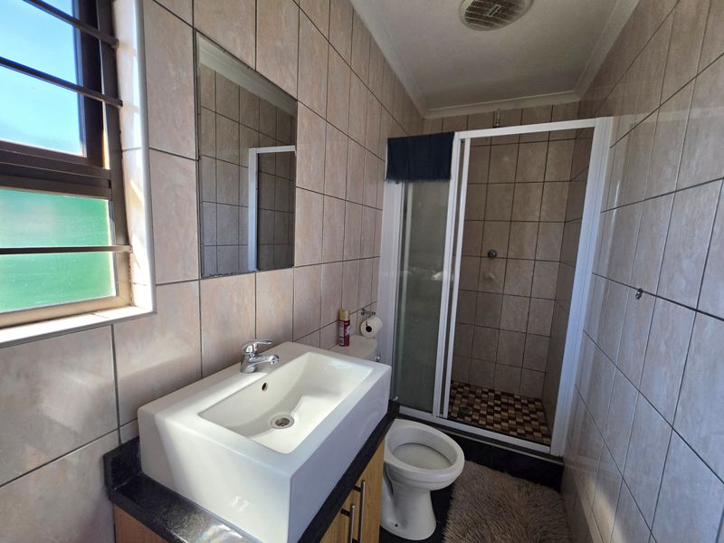 A functional bathroom featuring a vanity basin, a separate shower enclosure, and a toilet, finished with neutral wall tiling.