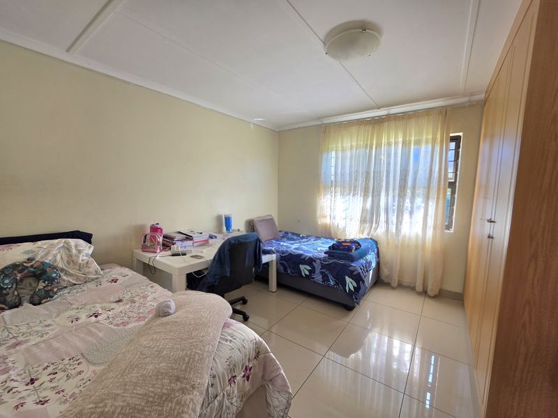 A functional bedroom featuring tiled flooring, built-in wooden cupboards, and a window with curtaining, providing a practical living space.