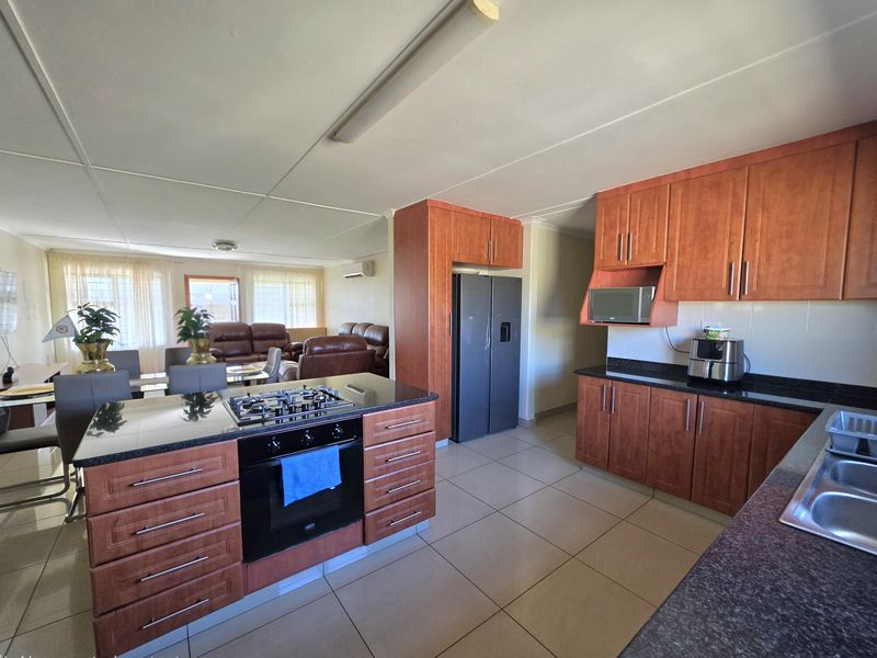 Open-plan kitchen and living area featuring wood-finish cabinetry, granite countertops, a central island with a gas hob, and tiled flooring throughout.