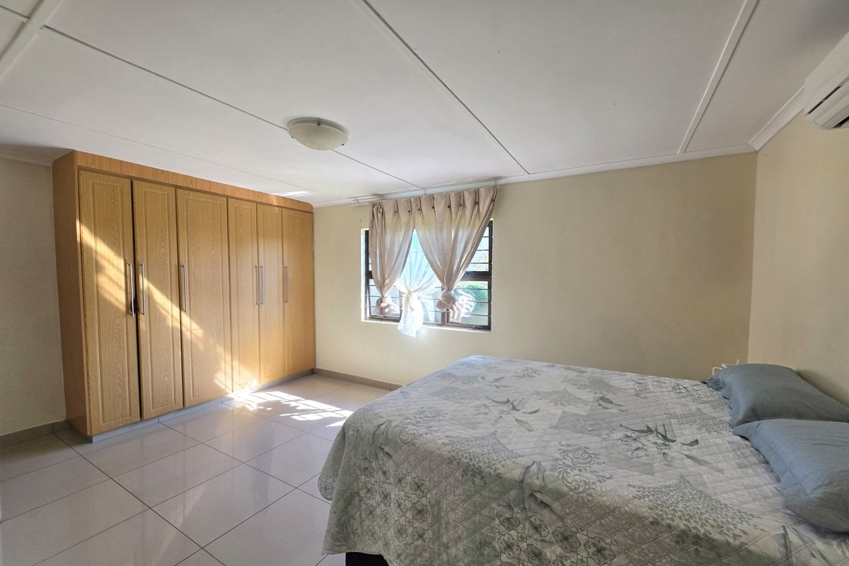 A well-maintained bedroom featuring neutral tiled flooring, ample built-in wooden cupboards, and a split-system air conditioning unit for climate control.