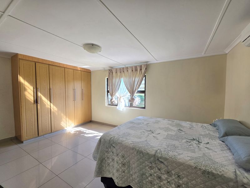 A well-maintained bedroom featuring neutral tiled flooring, ample built-in wooden cupboards, and a split-system air conditioning unit for climate control.