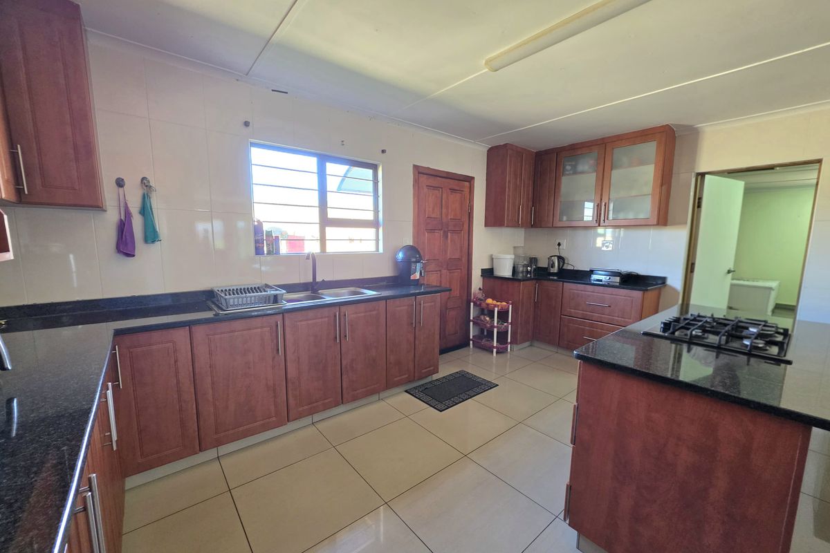 Spacious kitchen featuring dark granite countertops, ample wooden cabinetry, a gas hob, and tiled flooring throughout.