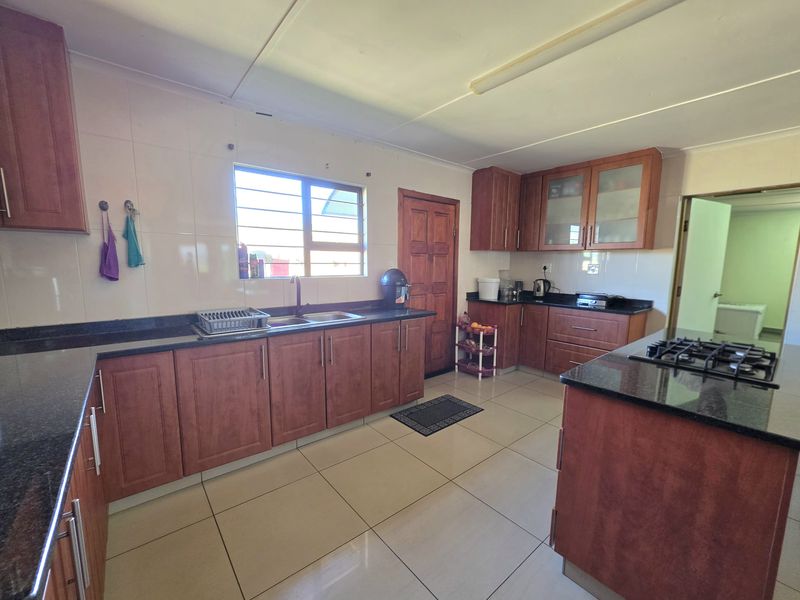 Spacious kitchen featuring dark granite countertops, ample wooden cabinetry, a gas hob, and tiled flooring throughout.