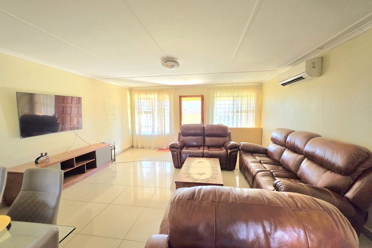 A spacious living room featuring tiled flooring, a wall-mounted air conditioning unit, and natural light through large windows.