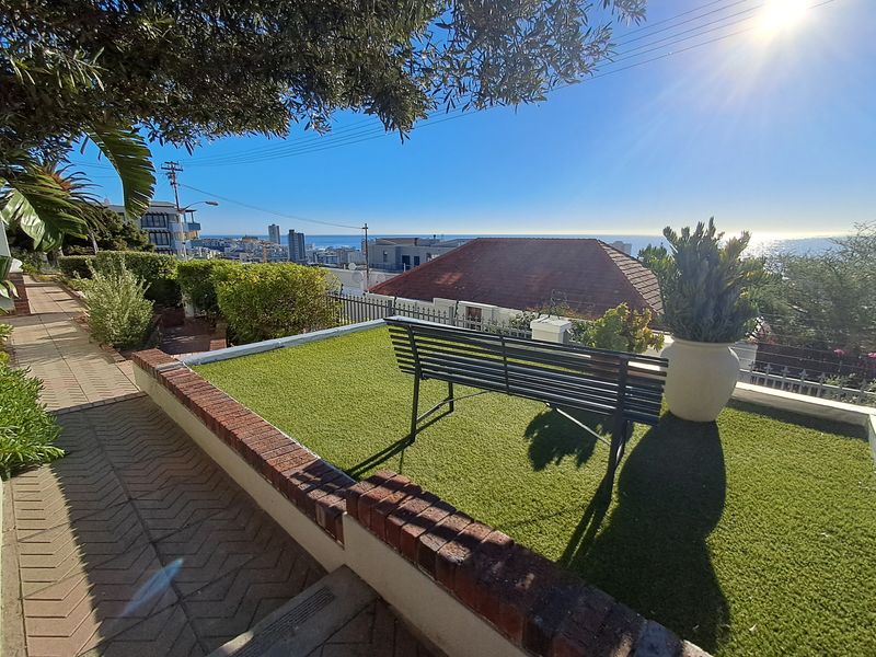 Elevated outdoor terrace featuring artificial turf, brick retaining walls, and panoramic coastal and city views.