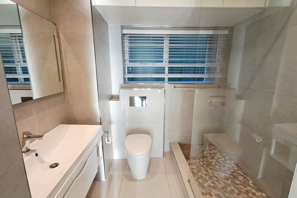 Modern bathroom featuring a sleek vanity, concealed cistern toilet, and a walk-in shower with a decorative pebble floor and glass screen.