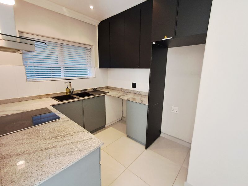 Modern kitchen featuring granite countertops, dark upper cabinetry, light lower cabinets, electric hob, extractor fan, and tiled flooring.