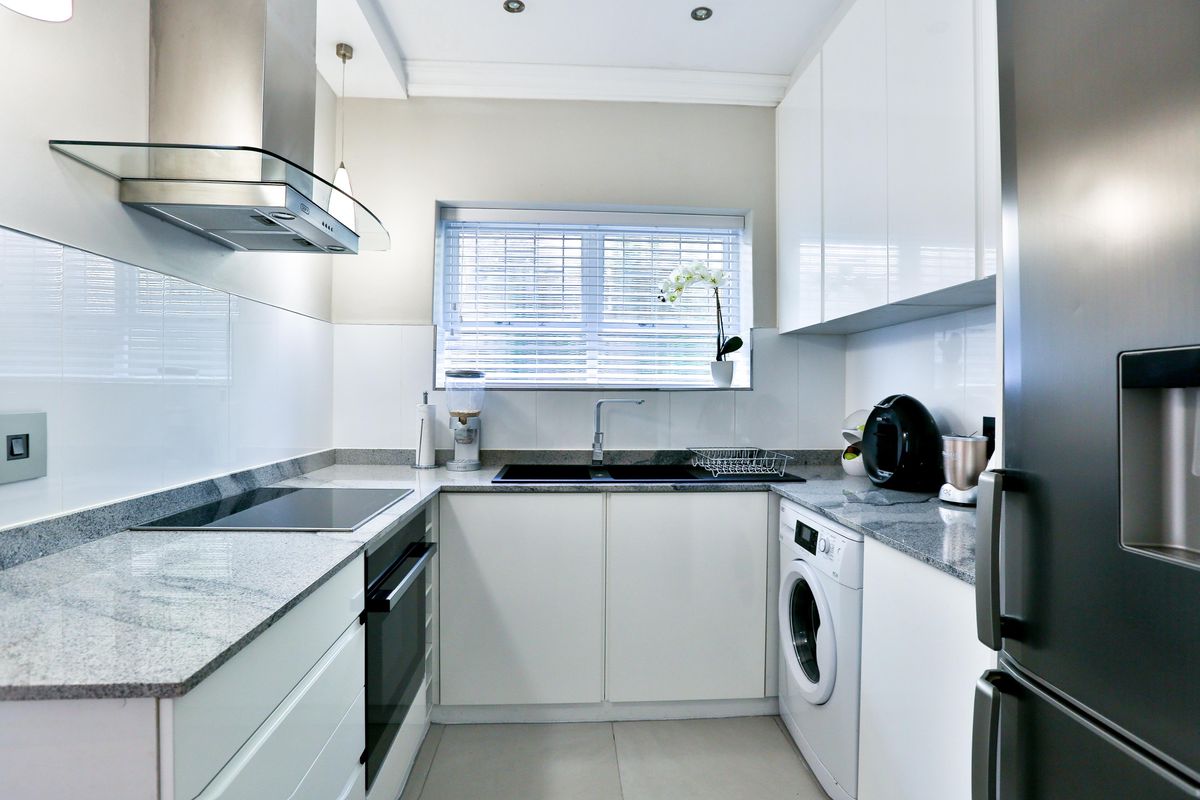 Modern galley-style kitchen featuring sleek white cabinetry, granite countertops, integrated appliances, and high-quality finishes throughout.