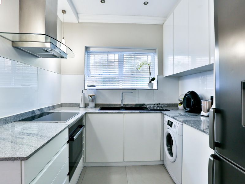 Modern galley-style kitchen featuring sleek white cabinetry, granite countertops, integrated appliances, and high-quality finishes throughout.