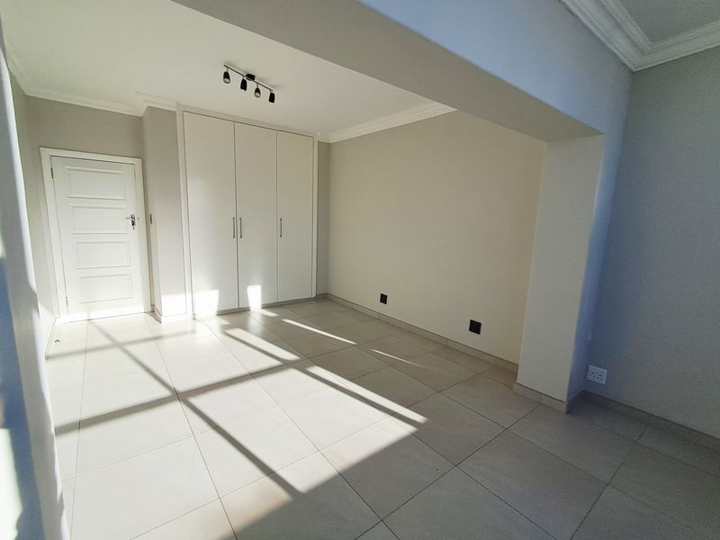 A bright, empty bedroom featuring neutral tiled flooring, built-in cupboards, and modern track lighting, offering a clean and versatile living space.
