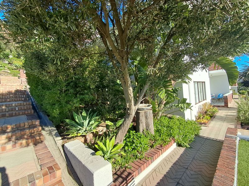 A well-maintained garden area featuring brick paved pathways, tiered brick retaining walls, and established greenery leading towards the apartment entrance.