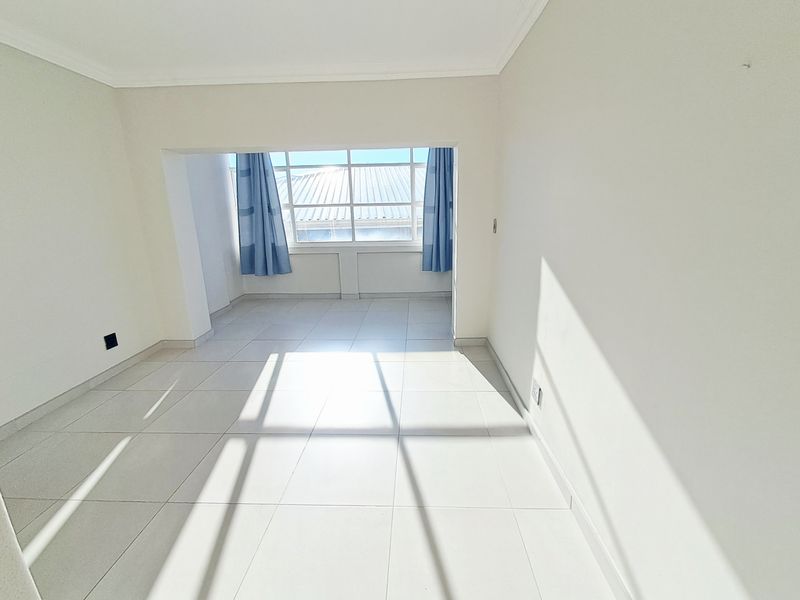 A bright, empty living area featuring neutral tiled flooring and a large window that allows for ample natural light.
