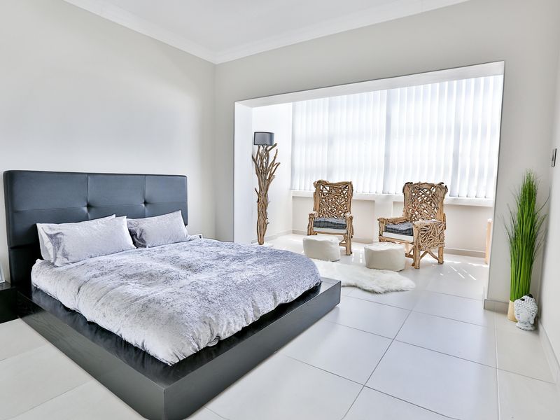 Spacious bedroom featuring neutral tiled flooring, coved ceilings, and large windows with vertical blinds, creating a bright and airy atmosphere.