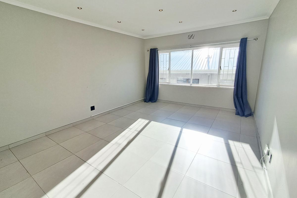 A bright, empty bedroom featuring neutral tiled flooring, recessed downlighting, and large windows with security bars.