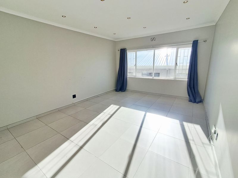 A bright, empty bedroom featuring neutral tiled flooring, recessed downlighting, and large windows with security bars.