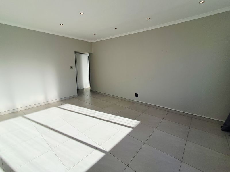 A bright, empty living area featuring neutral ceramic floor tiles, recessed downlighting, and a clean, minimalist aesthetic ready for personalization.