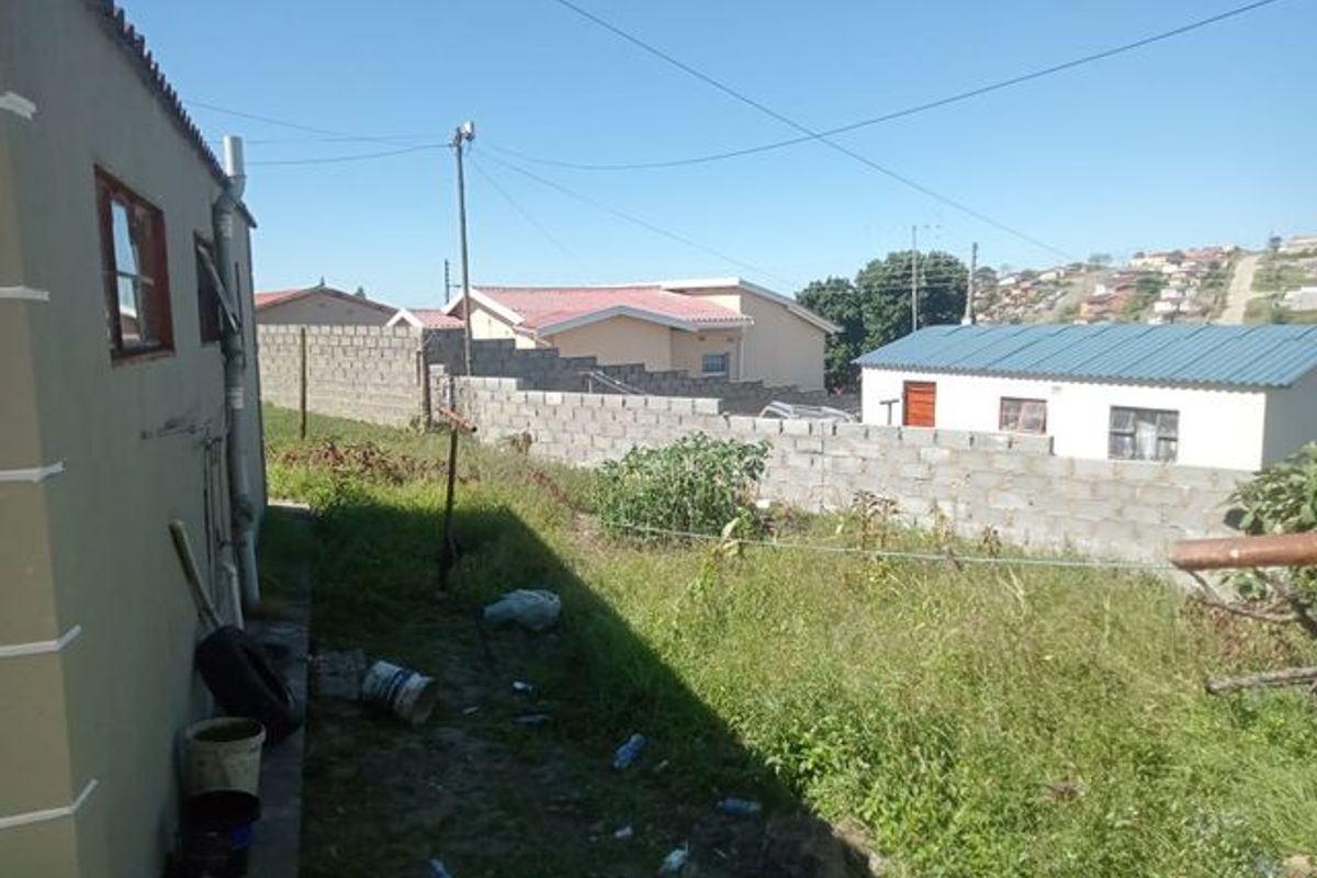 Rear exterior view of the property featuring a concrete block boundary wall and an unpaved garden area.