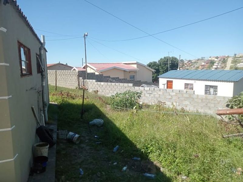 Rear exterior view of the property featuring a concrete block boundary wall and an unpaved garden area.