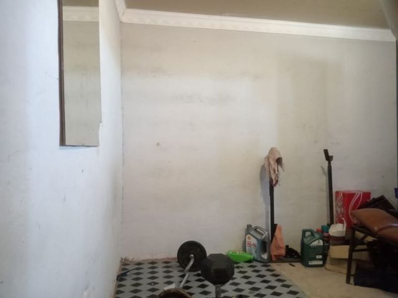 A functional garage space featuring tiled flooring and coving, currently used for storage with visible wear on the wall surfaces.