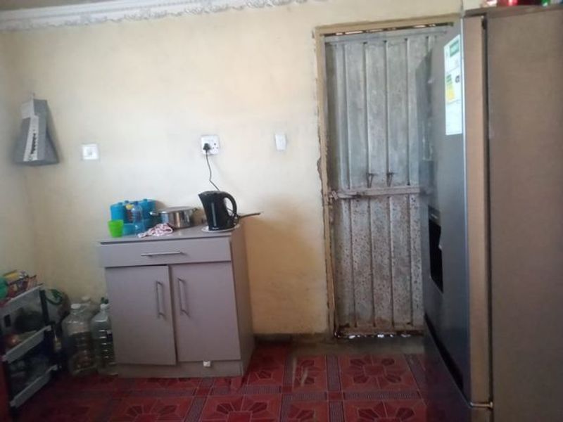 A basic kitchen area featuring tiled flooring, decorative cornice, and a metal security door, requiring cosmetic updates to improve the overall condition.