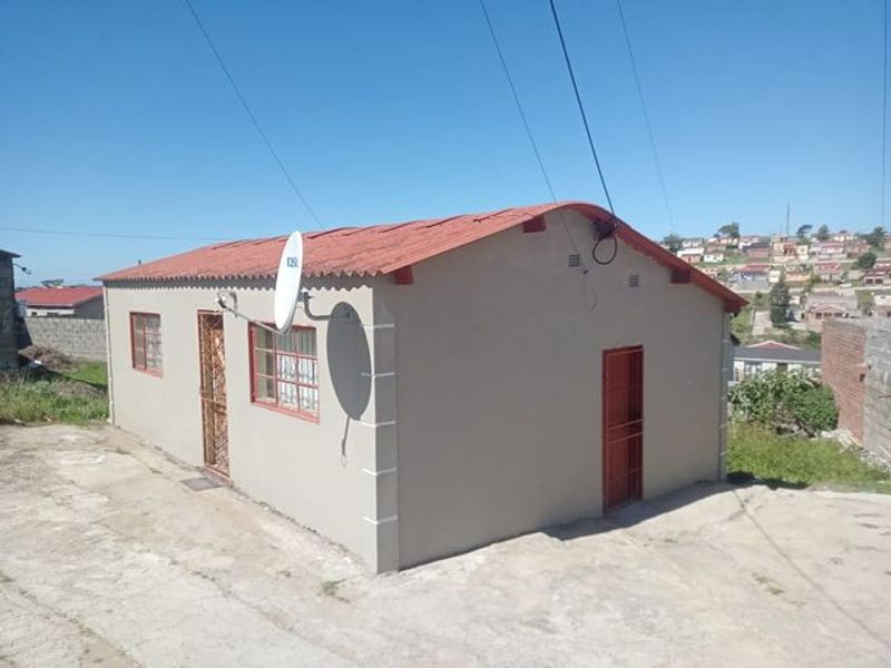 A single-story residential house featuring a corrugated metal roof, security gates, and security bars on windows, set on a concrete driveway.