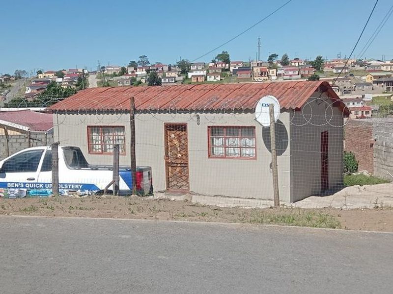 A detached single-story residential dwelling featuring a corrugated metal roof, security gate, and perimeter razor wire fencing.