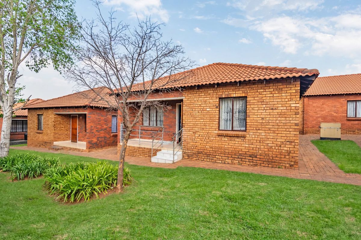Exterior view of a face brick townhouse featuring a terracotta tiled roof, paved walkways, and a small entrance porch with metal railings.