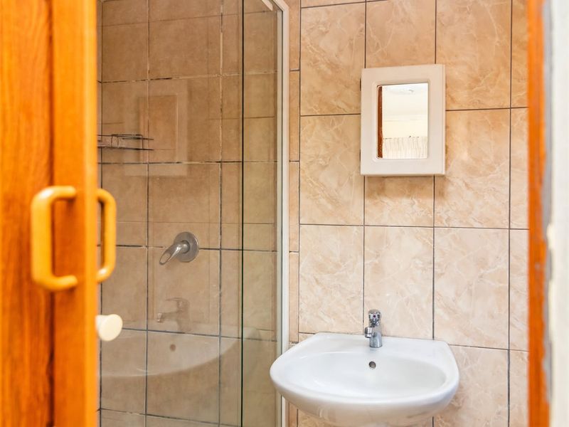 A compact bathroom featuring a glass-enclosed shower, wall-mounted basin with mixer tap, and neutral tiled wall finishes.