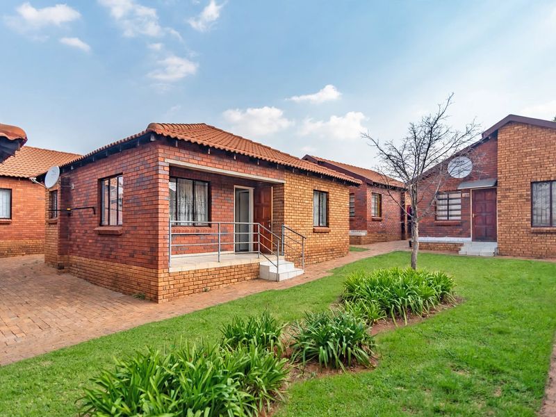 A well-maintained townhouse complex featuring face brick exteriors, tiled roofs, and paved walkways set within a landscaped garden area.