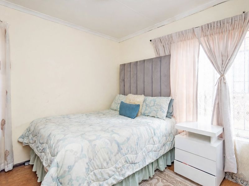 A cozy bedroom featuring laminate flooring, neutral wall tones, and window security bars, providing a functional and comfortable sleeping space.