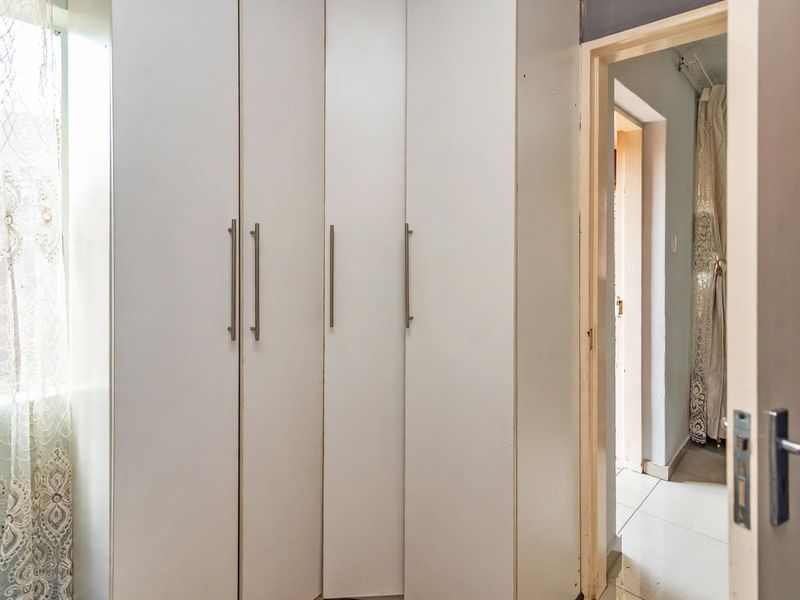 A bedroom interior featuring built-in cupboards and tiled flooring, leading into an adjacent hallway.