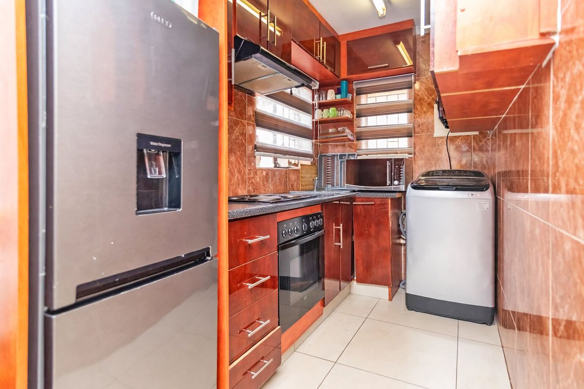 Compact kitchen featuring dark wood-finish cabinetry, tiled walls, built-in oven with hob, and extractor fan, providing a functional workspace.