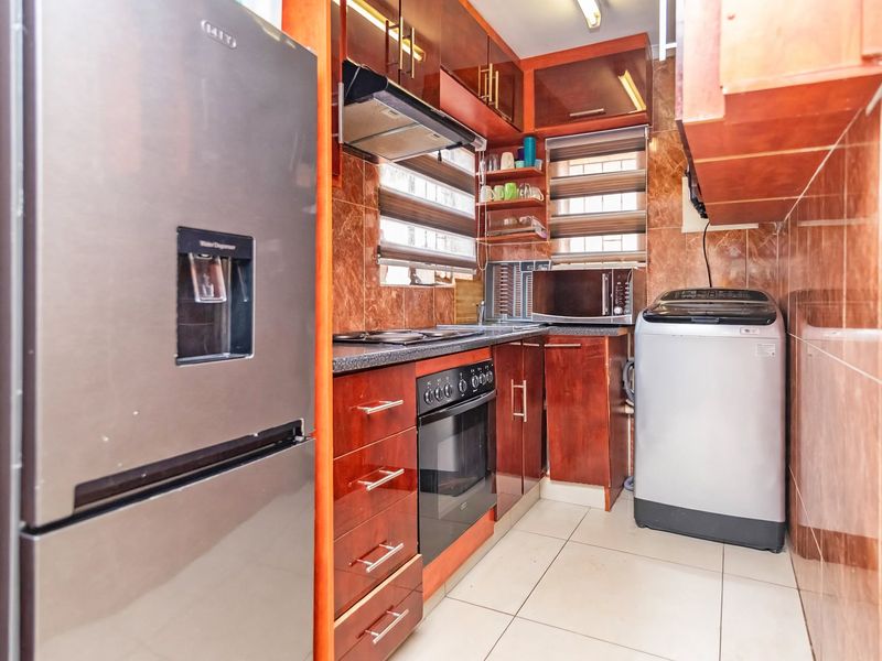 Compact kitchen featuring dark wood-finish cabinetry, tiled walls, built-in oven with hob, and extractor fan, providing a functional workspace.