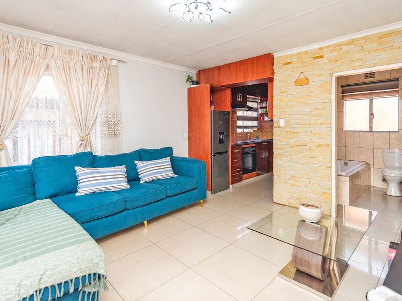 Open-plan living area featuring tiled floors, a stone-clad feature wall, and an integrated kitchen, with direct access to an adjacent bathroom.