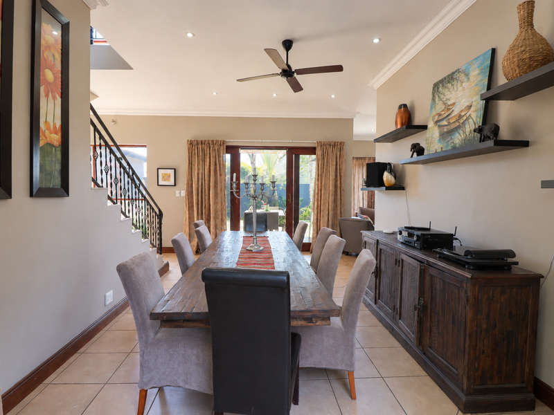 Spacious dining area featuring tiled flooring, crown molding, recessed lighting, and a wrought iron staircase, with direct access to the outdoor patio.